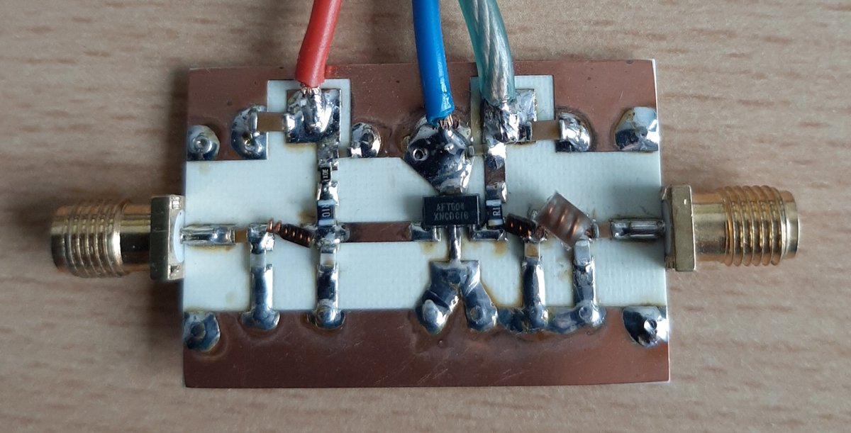 Foto eines selbst aufgebauten 2-W-Hochfrequenzverstärkers auf einer Platine mit zwei SMA-Buchsen für Ein- und Ausgang, einem Transistor in der Mitte, Spulen, Chip-Widerständen und drei angelöteten Versorgungskabeln in Rot, Blau und Grün.